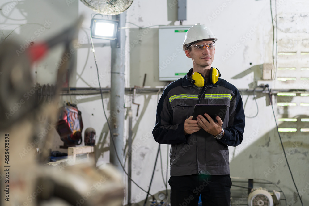Male engineer worker holding digital tablet working with welding robot arm in workshop. Male worker control automatic welding robot arm in factory. Industry robot manufacturing technology Male engineer worker holding digital tablet working with welding robot arm in workshop. Male worker control automatic welding robot arm in factory. Industry robot manufacturing technology