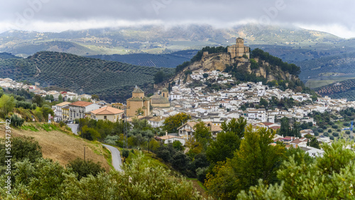 Ruins of a Moorish castle on a hilltop with houses filling the hillside and olive groves in the rolling hills; Montefrio, Province of Granada, Spain