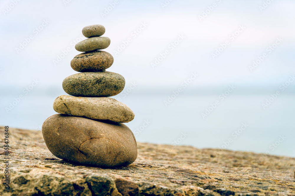Fototapeta premium Stacked stones on beach on the rock. Shape of a pyramid. Concept zen, harmony, balance. Selective focus.