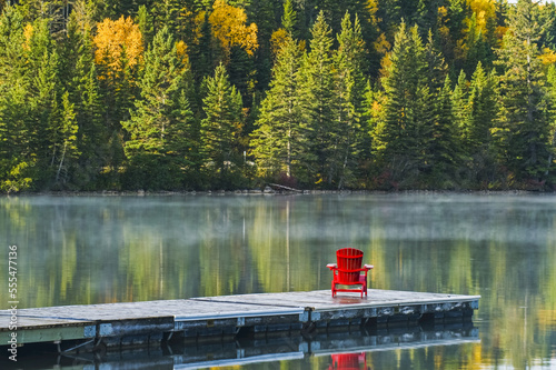 Muskoka chair on dock with autumn coloured foliage reflected in the tranquil lake water of Clear Lake, Riding Mountain National Park; Manitoba, Canada photo