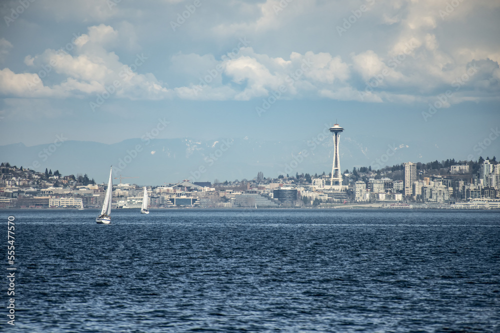 The city of Seattle and the iconic Space Needle as sail boats ply the waters of Elliott Bay. A warm spring day produces heat waves rising from the water; Seattle, Washington, United States of America The city of Seattle and the iconic Space Needle as sail boats ply the waters of Elliott Bay. A warm spring day produces heat waves rising from the water; Seattle, Washington, United States of America
