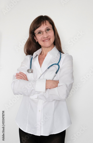 A woman of European appearance, a doctor in a mask, with a stethoscope, in a white coat on a light background. Clinic concept, specialist.