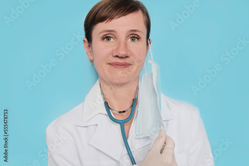 A woman of European appearance  a doctor in a mask  with a stethoscope  in a white coat on a light background. Clinic concept  specialist.