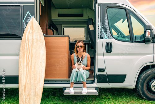 Young woman sitting with her boston terrier dog at the door of her camper van during a trip
