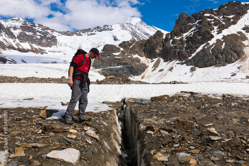 A hiker peers into a crevasse on Castner Glacier in the Alaska Range with Black Cap in the background; Alaska, United States of America photo