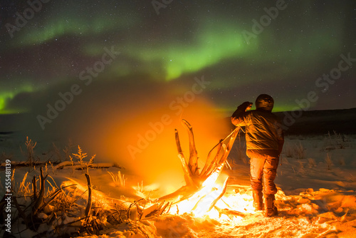 Staying warm beside a campfire on the Delta River while watching the aurora borealis on a frigid night; Alaska, United States of America