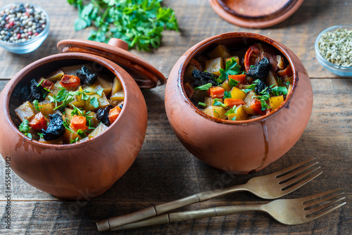 Obraz na plátně Stewed potato, carrot, onion, tomato and prunes in a clay pots with lid on woode