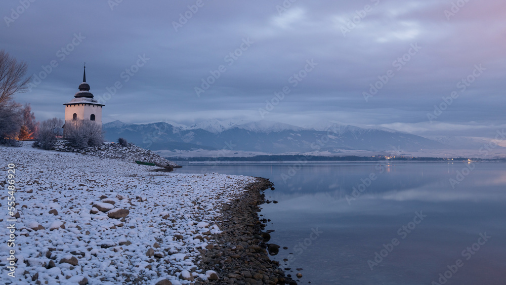 Fototapeta premium Church Tower of Virgin Mary at the shore of The Liptovska Mara dam in the morning light at winter, the area of Liptov in Slovakia