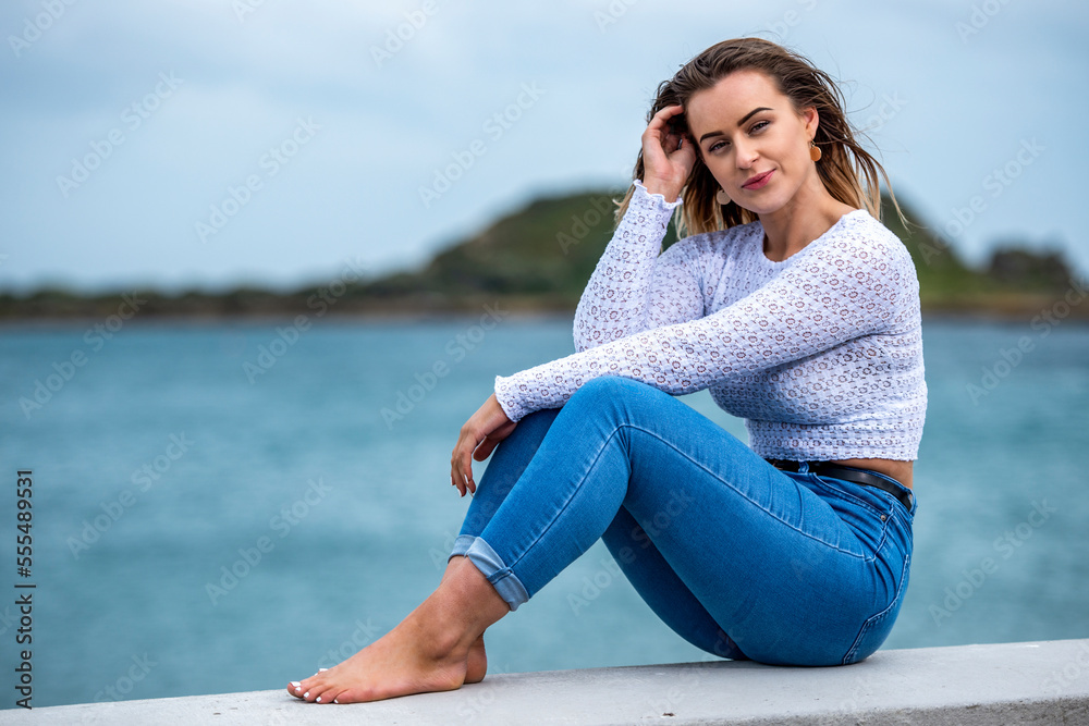 Portrait of a young woman sitting on a wall along the ocean; Wellington, North Island, New Zealand Portrait of a young woman sitting on a wall along the ocean; Wellington, North Island, New Zealand