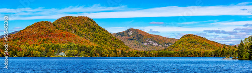 Vibrant autumn coloured foliage in a forest along a tranquil lake in the Laurentian Mountains; Lac Superieur, Quebec, Canada