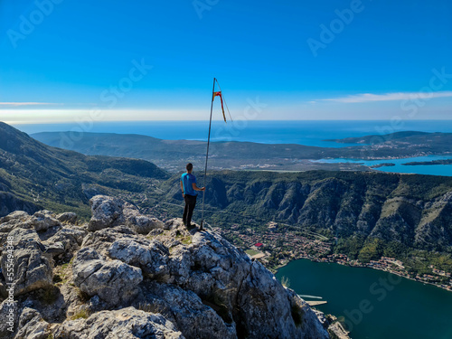 Man with panoramic view from Pestingrad (Derinski Vrh) of Kotor bay in sunny summer, Adriatic Mediterranean Sea, Montenegro, Balkan, Europe. Fjord winding along coastal towns. Lovcen, Orjen mountains