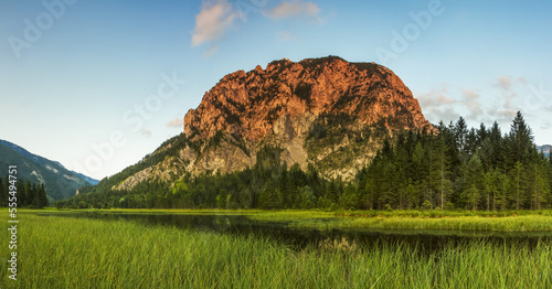 Cliff face on alpine mountain being hit with a summer evening sun, overlooking a lake and forest; Wildaplen, Landl, Austria photo