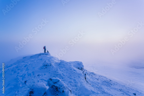 Man and dog hiking on top of snow-covered mountain in fog in the winter, Galty Mountains; County Tipperary, Ireland photo