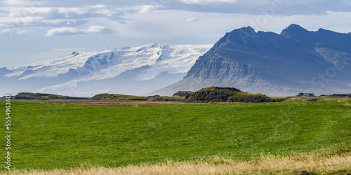 Landscape in Southeastern Iceland with rugged mountains and grass field, and snow-covered mountains in the distance; Hornafjorour, Eastern Region, Iceland photo