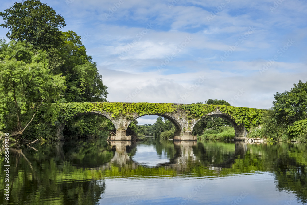 Old stone bridge over the Blackwater river in Kilavullen reflected in the water on a sunny summer day; Killavullen, County Cork, Ireland Old stone bridge over the Blackwater river in Kilavullen reflected in the water on a sunny summer day; Killavullen, County Cork, Ireland