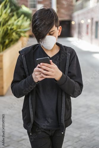 Tween male using his smart phone and wearing a protective mask to protect against COVID-19 during the Coronavirus World Pandemic; Toronto, Ontario, Canada photo