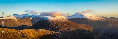 Panoramic view of the morning sun rays hitting the MacGillycuddy's Reeks covered in snow in winter, stiched panoramic; County Kerry, Ireland photo
