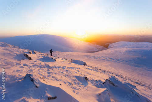 A lone man hiking down the snow-covered slopes of the Galty mountains at sunrise; County Tipperary, Ireland photo