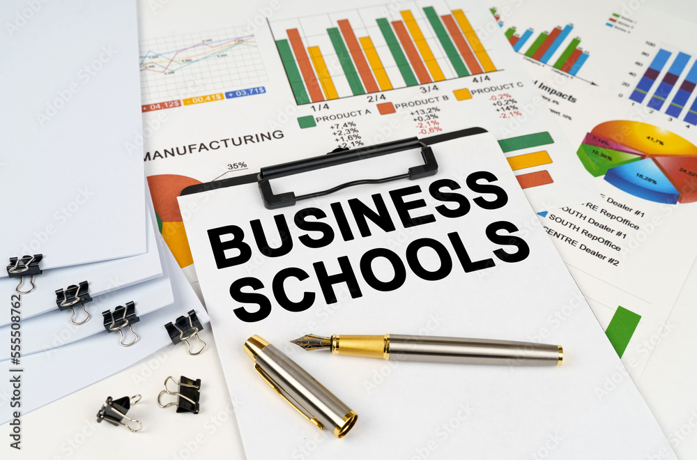On the table among financial graphs and charts lies a tablet with the inscription - Business Schools On the table among financial graphs and charts lies a tablet with the inscription - Business Schools