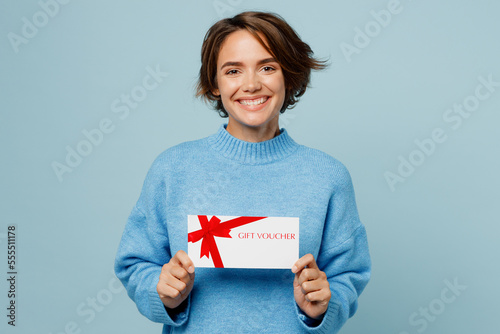 Young cheerful happy smiling woman in knitted sweater hold gift certificate coupon voucher card for store isolated on plain pastel light blue cyan background studio portrait People lifestyle concept. photo