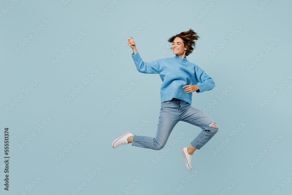 Full body smiling musician happy fun young woman wear knitted sweater jump hgh play guitar hand gesture isolated on plain pastel light blue cyan background studio portrait. People lifestyle concept.