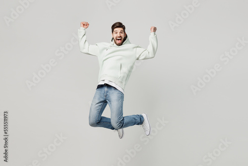 Full body young overjoyed excited satisfied fun caucasian man wear mint hoody look camera jump high do winner gesture isolated on plain solid white background studio portrait People lifestyle concept