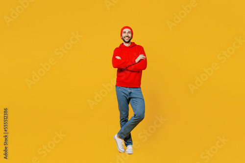 Full body confident smiling cheerful young caucasian man wear red hoody hat look camera hold hands crossed folded isolated on plain yellow color background studio portrait. People lifestyle concept.