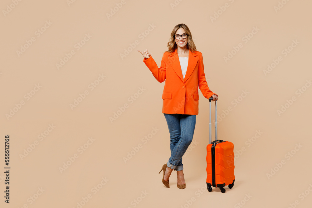 Full body traveler business woman in formal orange suit glasses hold bag point aside isolated on plain beige background studio Tourist travel abroad in free time rest getaway Air flight trip concept Full body traveler business woman in formal orange suit glasses hold bag point aside isolated on plain beige background studio Tourist travel abroad in free time rest getaway Air flight trip concept