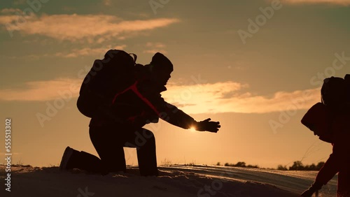 Working in team of business people, Traveler climbs snowy peak. Team of businessman is going to win. Silhouettes of climbers give each other helping hand, climbing to top of snowy mountain, hill photo