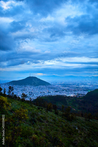 mountain in middle of a city with cloud sky, and green mountain in foreground, cerro del chiquihuite view from sierra de guadalupe photo