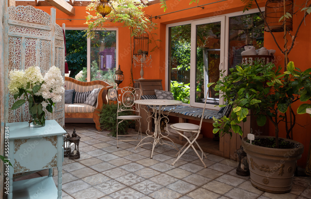 Interior of veranda. Cozy space in patio. A lot of plants. Orange wall. Wooden vintage furniture.