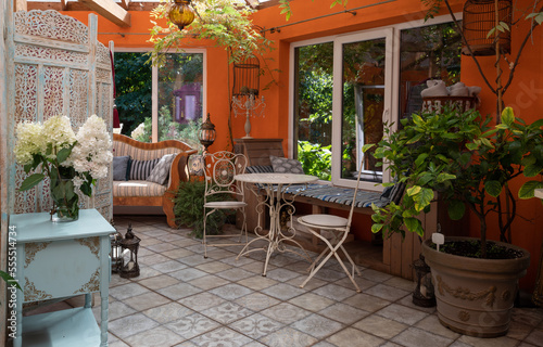Interior of veranda. Cozy space in patio. A lot of plants. Orange wall. Wooden vintage furniture.