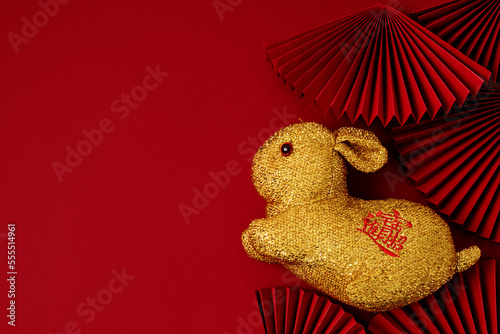 Golden rabbit over red background with paper fans. Text on hare means wishing of fortune, money, prosperity. Lunar new year concept
