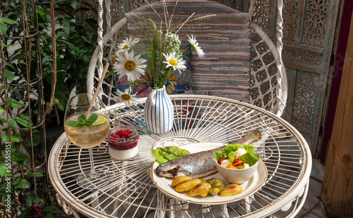 Fish, baked potatoes and fresh salad on a plate. Berry dessert. Drink in glass. Flowers in vase. Close-up of tasty food in cafe or restaurant photo