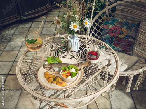 Fish, baked potatoes and fresh salad on a plate. Berry dessert. Drink in glass. Flowers in vase. Close-up of tasty food in cafe or restaurant photo