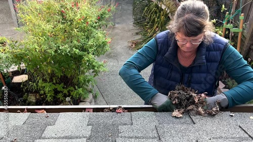 4K HD video of Older female on a ladder cleaning autumn leaves out of rain gutters. A debris clogged gutter can cause a leaky roof or water damage to the interior or exterior of your home.

