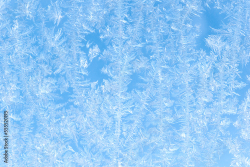 Blue background. Beautiful pattern of frost on the window against the blue sky.