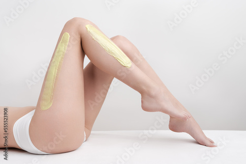 Beautiful woman legs while she lying down on couch during depilation process with green hot wax in professional beauty salon. Side view of slim young women body in white panties. Part of photo series.