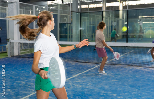 Teenager girl plays padel with partners. Back view
