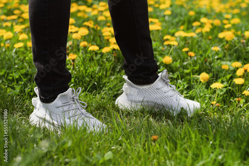 Bright modern and comfortable fabric sneakers of a teenager boy standing in the grass in spring and testing the sneakers for strength and comfort