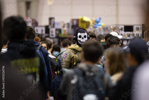 A male cosplayer in a military uniform and skull mask stands in the middle of a crowd of other visitors to the festival of games