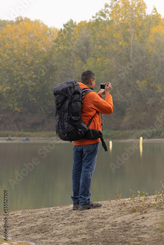 Portrait of traveler man at lake in autumn taking a photo with the digital camera and orange jacket