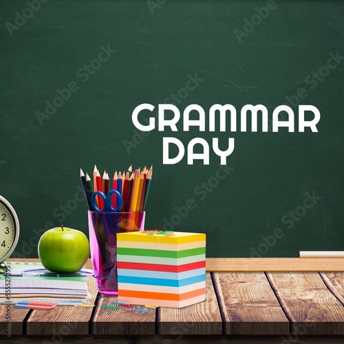 School equipment on wooden table against grammar day text on blackboard