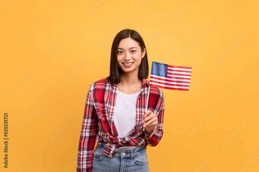 Education abroad, studying in the US, emigration concept. Happy asian female student holding american flag - obrazy, fototapety, plakaty 