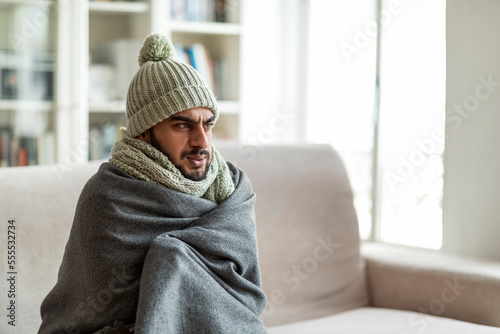 Murais de parede Freezing middle eastern guy sitting on couch in living room