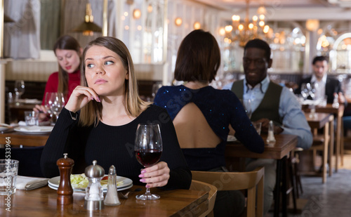 Portrait of thoughtful attractive girl with wine glass dining all alone in cozy restaurant .