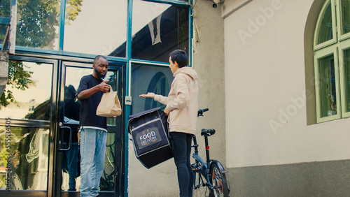 Confused delivery worker giving wrong fastfood order to customer, unsatisfied man acting displeased about restaurant takeaway problem. Food delivery service worker with backpack on bicycle.