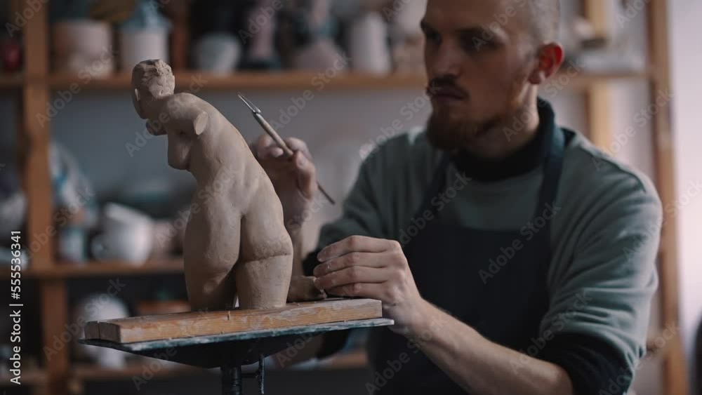 Skilled potter sculptor carefully working on a clay female statue with pottery loop in crafts studio Skilled potter sculptor carefully working on a clay female statue with pottery loop in crafts studio