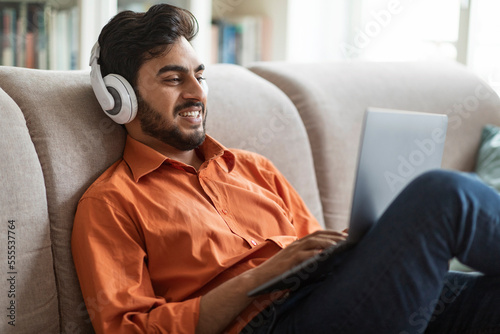 Relaxed arab guy watching movile on laptop, home interior photo