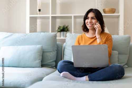 Remote Business. Arab Woman Talking On Phone And Using Laptop At Home